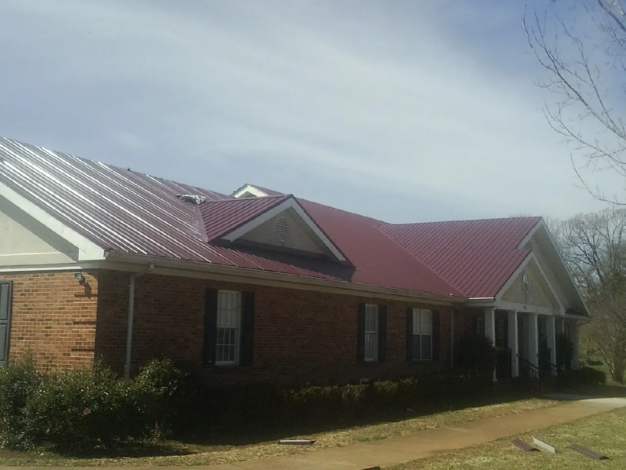 Red metal roof with gabled entries on a long brick building, from a Hail Damage Roof Repair job in Negley