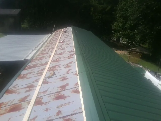 Old rusted panels beside newly installed green metal roofing — Wind Damage Roof Repair by Roofing Brothers in Negley