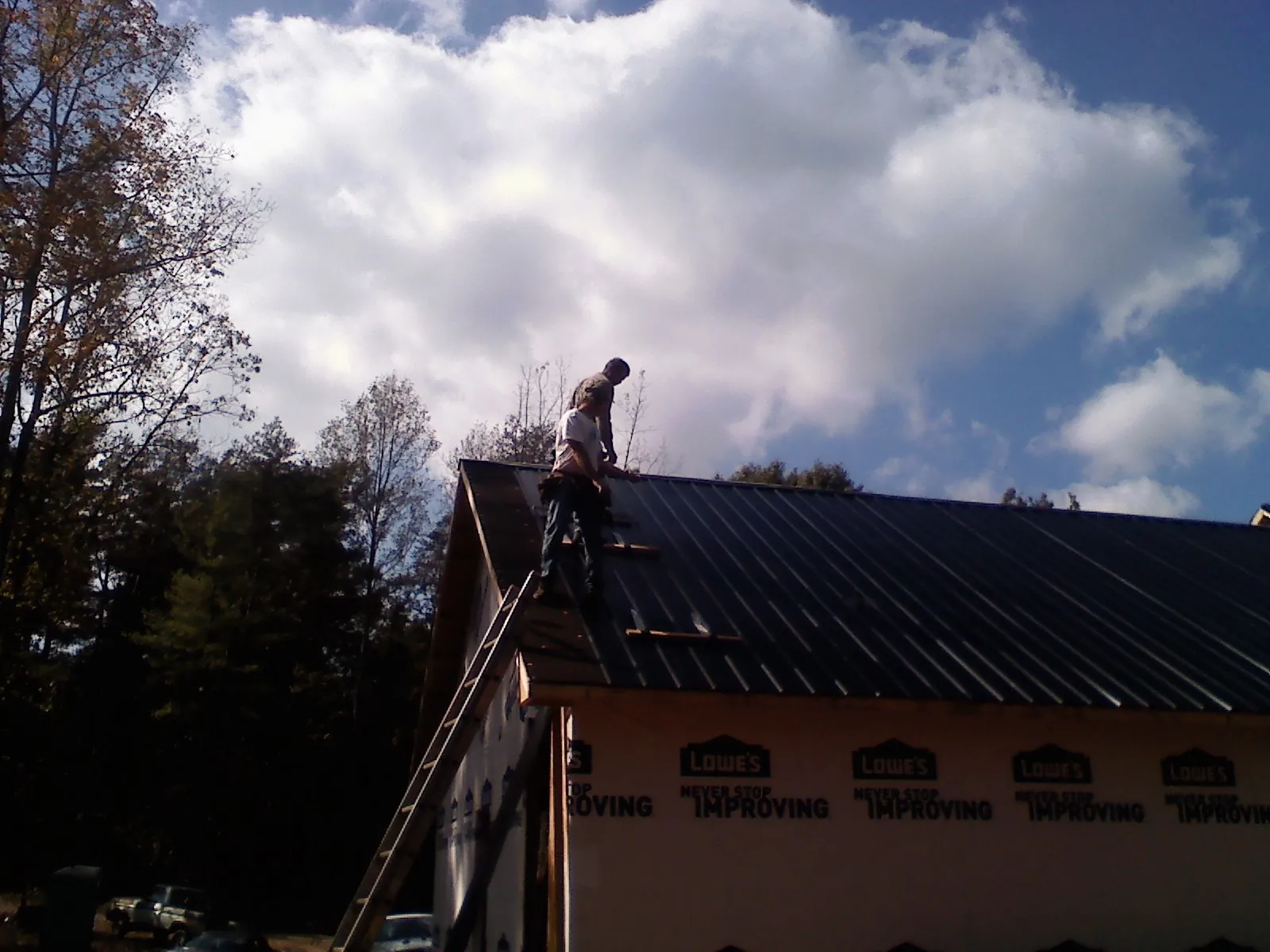 Roofer fastening dark metal panels high against a cloudy sky, from a Roof Inspection job in Negley