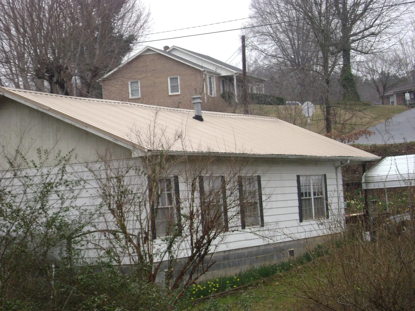 Tan metal roof on a white sided house set into a hillside — Commercial Roofing by Roofing Brothers in Negley