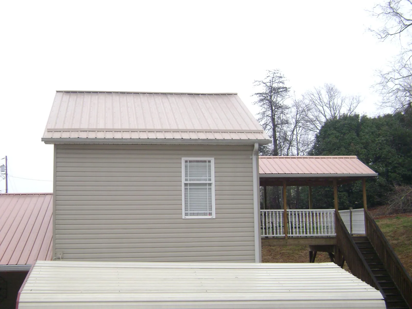Tan metal roofs on a two story addition and attached porch, from a Roof Replacement job in Negley